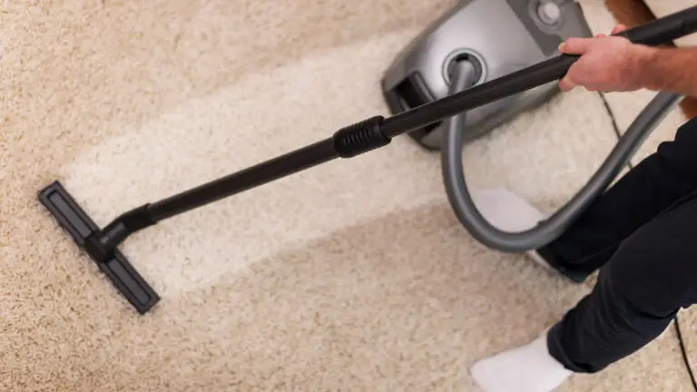 Person vacuuming a beige rug to demonstrate effective carpet cleaning tips.
