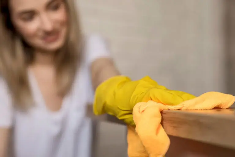 Woman cleaning a surface with a yellow glove, promoting mental health through tidy spaces.