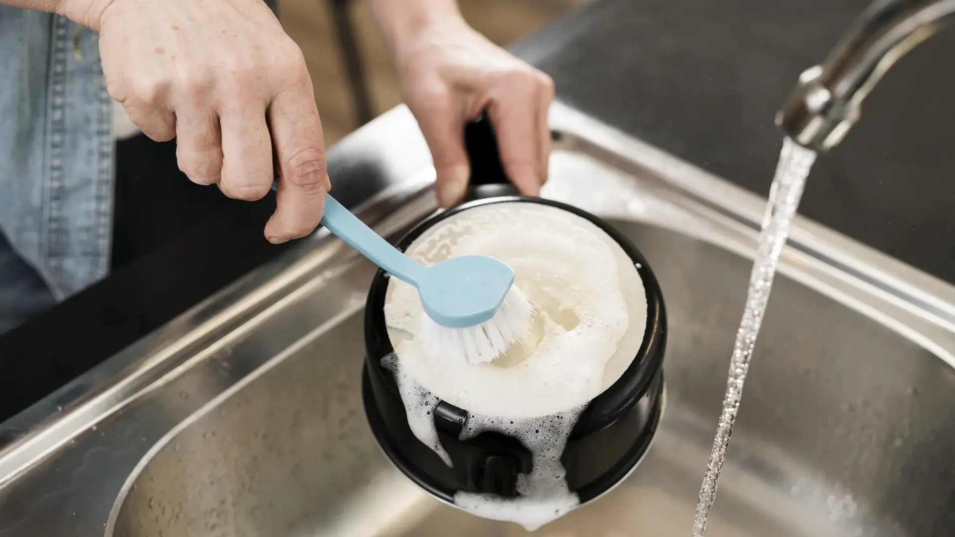 Hands scrubbing a pot with dish brush