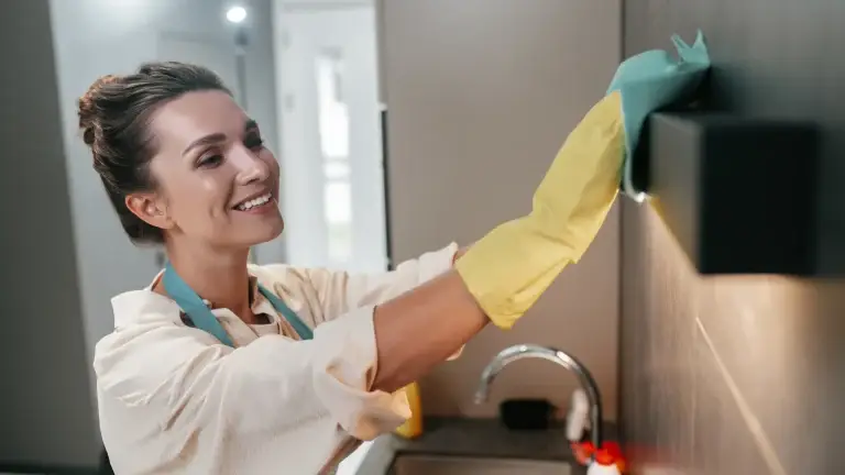 Two smiling cleaners with yellow gloves scrubbing a kitchen counter