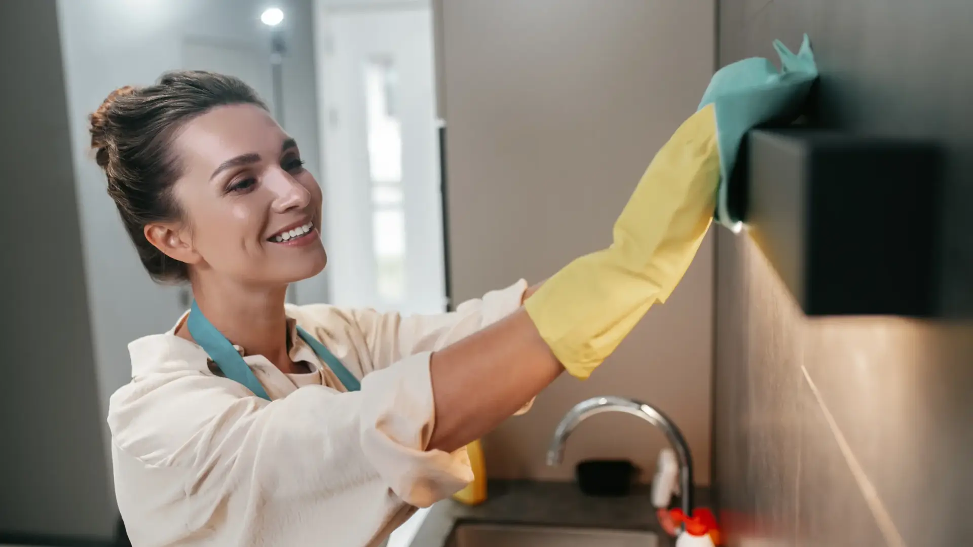 Two smiling cleaners with yellow gloves scrubbing a kitchen counter